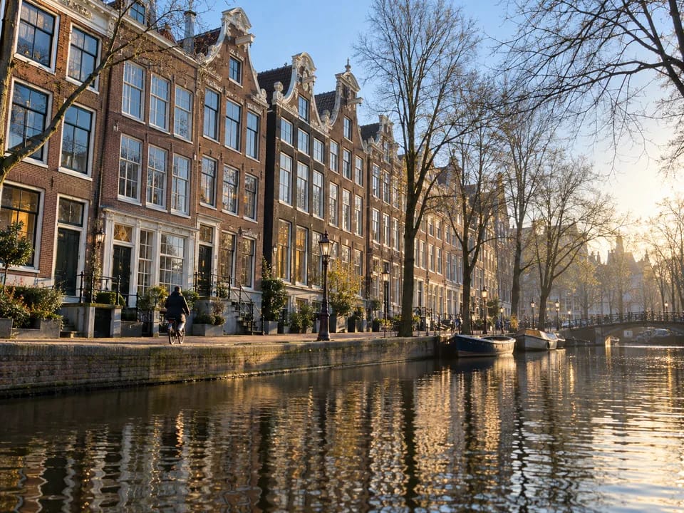 Brick canal house facades in Amsterdam reflected in the water, with a cyclist seen from behind, real estate participations with blockchain in the Netherlands