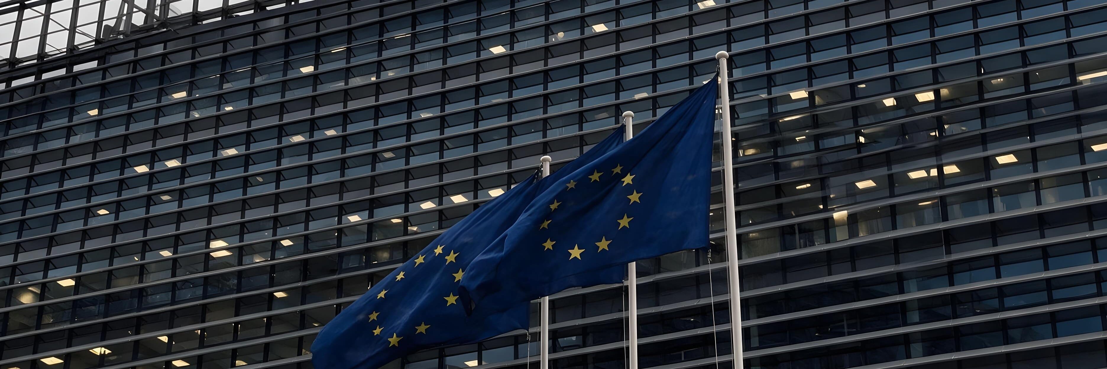 Three European Union flags against the lit office façade of the European Commission