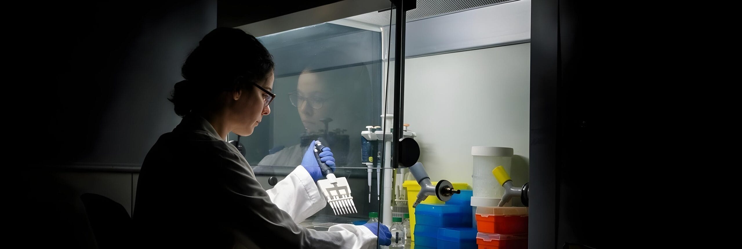 Researcher using a multichannel pipette inside a pharmaceutical laboratory hood